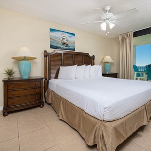 Master bedroom featuring a king bed, stylish wooden furniture, and a balcony with a view of the beach