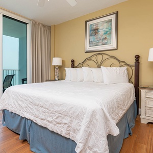 The master bedroom features a plush king bed, coastal decor, and a private balcony with a stunning beachfront view