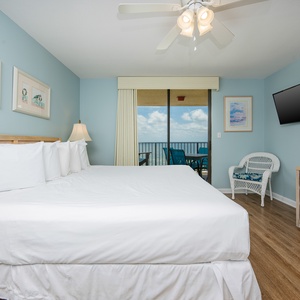 The master bedroom features a king bed, a wall-mounted TV, and balcony with a view of the beach