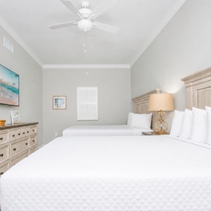 Serene guest bedroom featuring two comfortable queen beds, a large TV, and soft decor