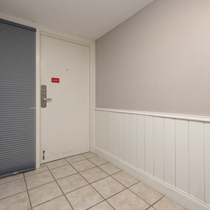 The entryway features a clean tile floor, light gray walls, and a door with a security lock, welcoming guests into the condo