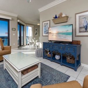 Cozy living area features a large TV, comfortable seating, and a view of the beach through expansive glass doors