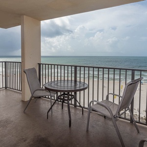 A private balcony features a round table and chairs, offering a serene view of the beach and tranquil waves