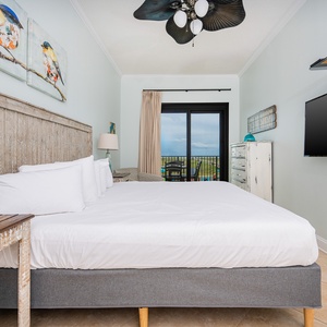 Cozy master bedroom features a king bed, stylish decor, and a balcony offering a view of the beach and the surrounding area