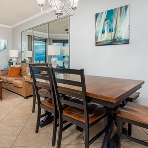 Living area features a brown leather sofa, dining table for four, and expansive views of the beach through large windows