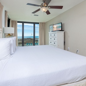 Spacious bedroom featuring a comfortable king bed, a TV, and large windows with a view of the beach