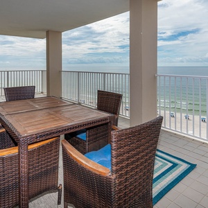 This balcony features a wooden dining table surrounded by wicker chairs, offering a stunning beachfront view