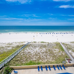 The view showcases a pristine beach with white sand, dotted with colorful umbrellas and sun loungers under a clear blue sky