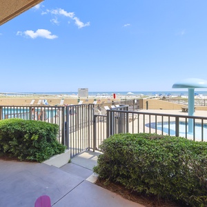 Enjoy the inviting view of the pool area and beach from your ground floor patio, surrounded by lush greenery