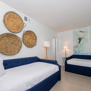 This guest bedroom features two stylish blue twin beds with trundles, elegant wall art, and warm lighting for a relaxing stay