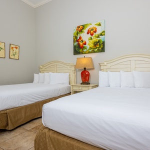 The guest bedroom features two comfortable queen beds, colorful floral artwork, and a stylish lamp for a cheerful atmosphere