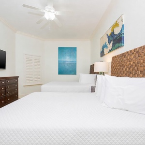 This guest bedroom features two queen beds, a flat-screen TV, and vibrant artwork, creating a relaxing atmosphere