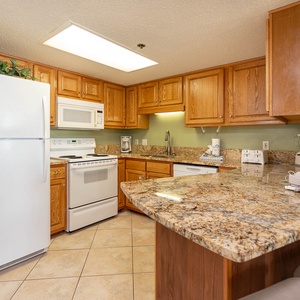 Prepare meals in this kitchen with ample counter space, wooden cabinetry, and white appliances