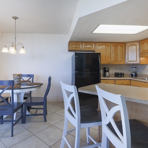 The kitchen features light wood cabinetry, a black refrigerator, and the dining area with a round table and blue chairs
