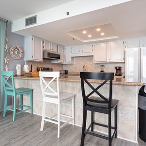 The kitchen features sleek cabinetry, granite countertops, stainless appliances, and a breakfast bar with colorful stools
