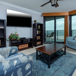 Cozy living area features a blue sofa with queen sleeper, a wooden coffee table, and expansive views of the beach