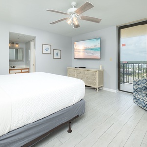 Brightly lit master bedroom featuring a plush king bed, a TV on a light wood stand, and access to a private balcony