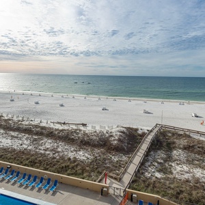 Enjoy a serene view of the beach with soft white sand and gentle waves, framed by a relaxing pool area below