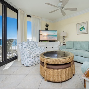 Cozy living area features a teal sofa, starfish-patterned chair, flat-screen TV, and a view of the beach