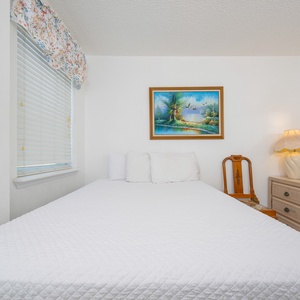The guest bedroom features a bed with elegant bedding, a charming lamp, and a scenic artwork above, creating a serene retreat