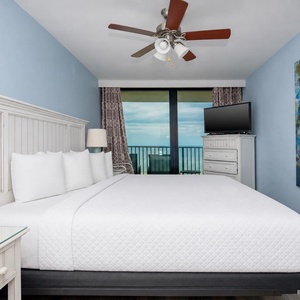 This bedroom features a king-sized bed, a colorful abstract painting, and a TV, with a stunning beachfront view