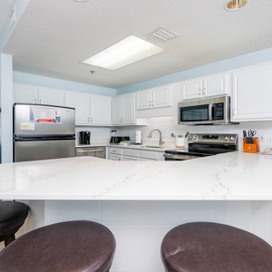 The kitchen features white cabinetry, coffee station, a spacious breakfast bar with seating, and stainless appliances