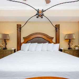 The master bedroom features a beautifully crafted wooden king bed, stylish lamps, and soft white linens for a restful stay