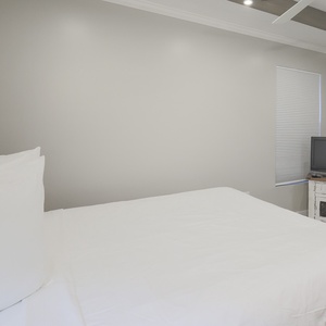 This guest bedroom features a cozy red bed, a TV for entertainment, and a bright atmosphere with natural light