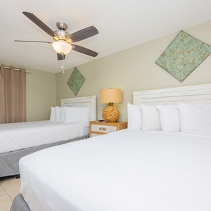 Two queen beds with white linens, decorative wall art, and a stylish lamp create a welcoming atmosphere in this guest room