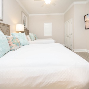 Cozy guest bedroom with two queen beds, a large TV, and relaxing coastal vibe