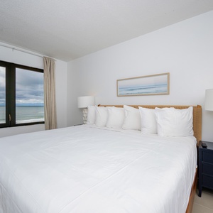 This bedroom features a king-sized bed, soft white linens, and a stunning beachfront view through large windows