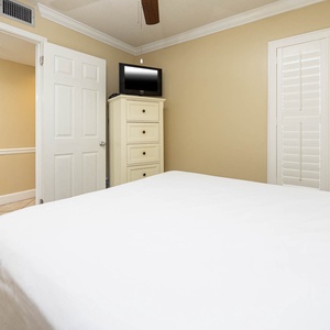 This cozy guest bedroom features a light-colored decor, a TV for entertainment, and easy access to a bathroom