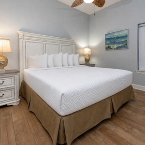Bedroom featuring a king bed with decorative pillows, a stylish nightstand, and a beach-themed painting on the wall