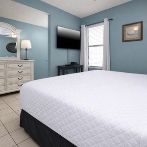 This bedroom features a comfortable bed, a large TV, and charming decor with a soothing blue wall color
