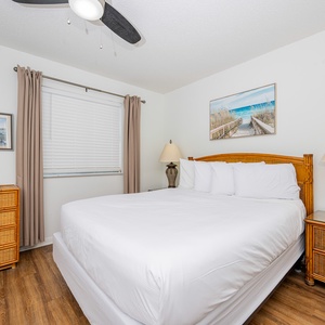 This bedroom features a comfortable queen bed, warm wood accents, and a serene beach-themed artwork for a relaxing stay