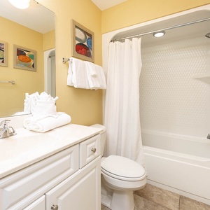 Calming guest bathroom featuring a clean tub/shower combo, fresh towels, and colorful artwork on the walls