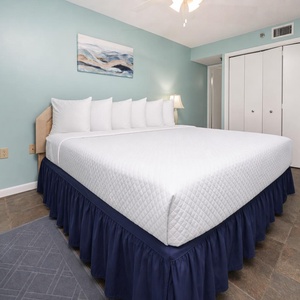 The guest bedroom features a king bed with crisp white linens, a light blue accent wall, and a stylish dresser for storage