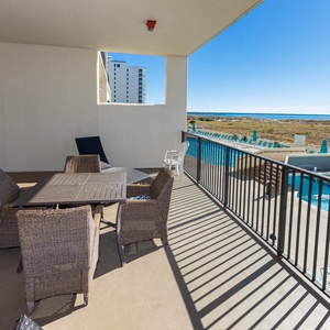 Spacious balcony with a outdoor patio set overlooks the pool area and offers a glimpse of the beach beyond