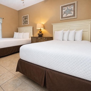 Guest bedroom featuring two queen beds with plush white linens, warm tones, and coastal-themed artwork