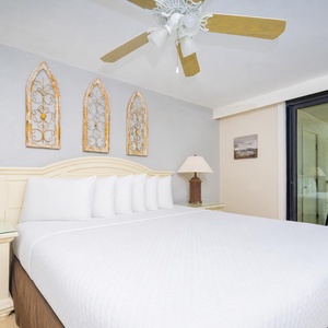 The master bedroom features a plush king bed, decorative wall art, and a balcony with a beautiful view of the beach