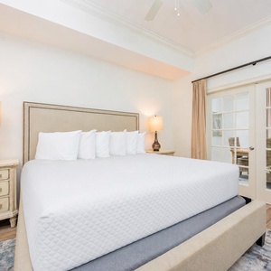 The master bedroom features a plush king bed with crisp linens, leading to a bright dining area through glass doors