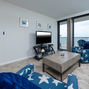 This inviting living area features a large TV, beach-themed decor, and a stunning view of the coastline from the balcony