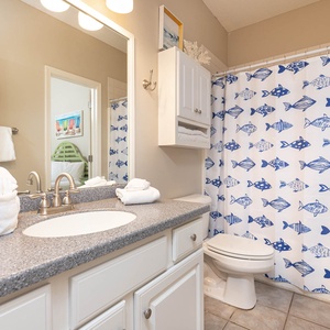 Bright bathroom featuring a granite countertop, decorative fish-patterned shower curtain, and fresh towels