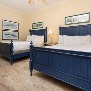 This guest bedroom features two blue queen beds, soft linens, and charming artwork, creating a relaxing atmosphere