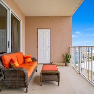 Enjoy a relaxing moment on the balcony with orange cushions, overlooking the beach and charming coastal homes