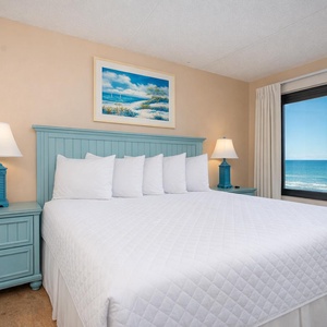 King master suite with a cozy bed, ample pillows, and a stunning beachfront view from the large windows