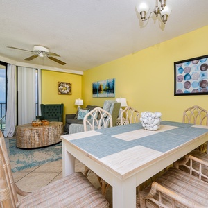 Brightly colored living area featuring a cozy sofa, dining table, and large windows showcasing a beautiful beachfront view