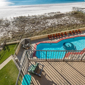 A view from the balcony showcases a sparkling pool surrounded by lounge chairs and a pristine beach just beyond