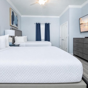 Relax in this inviting guest bedroom featuring two queen beds, a large TV, and stylish decor