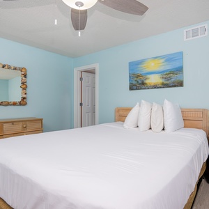 The bedroom features a bed with plush pillows, a seashell mirror, and a colorful beach scene painting for a relaxing stay
